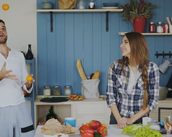 Attractive loving couple having fun in the kitchen. Handsome man juggle with fruits to impress his girlfriend at home